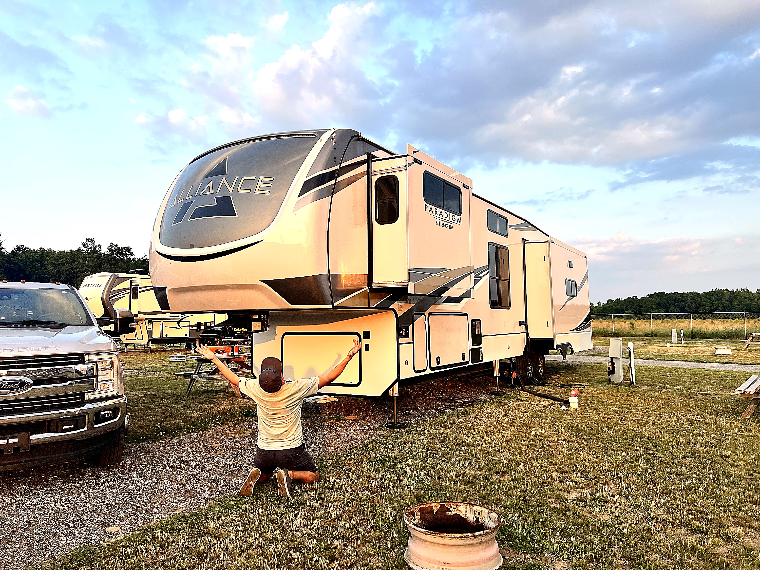David on his knees in front of his Alliance Paradigm fifth-wheel at sunset