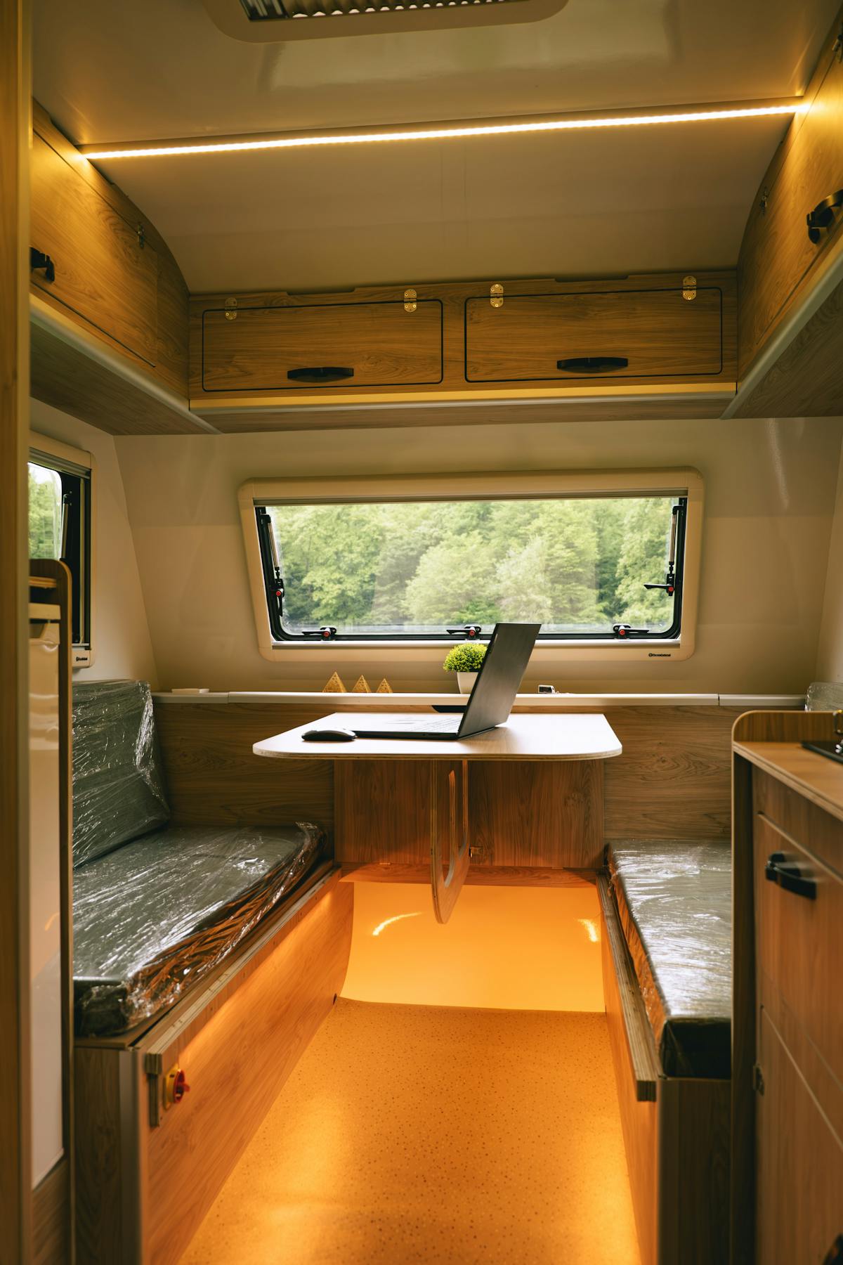 A laptop on an RV table with forest visible through the window.
