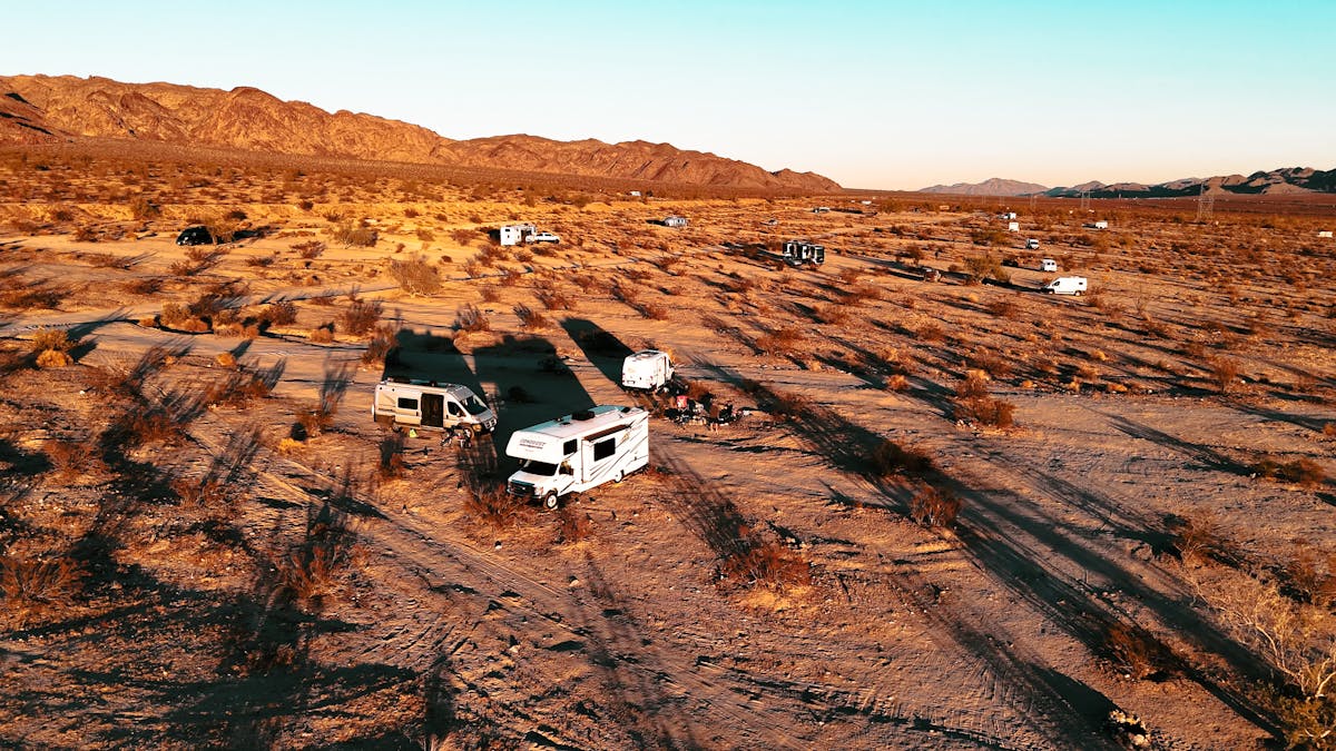 An aerial view of multiple RVs clustered in a desert valley at golden hour.
