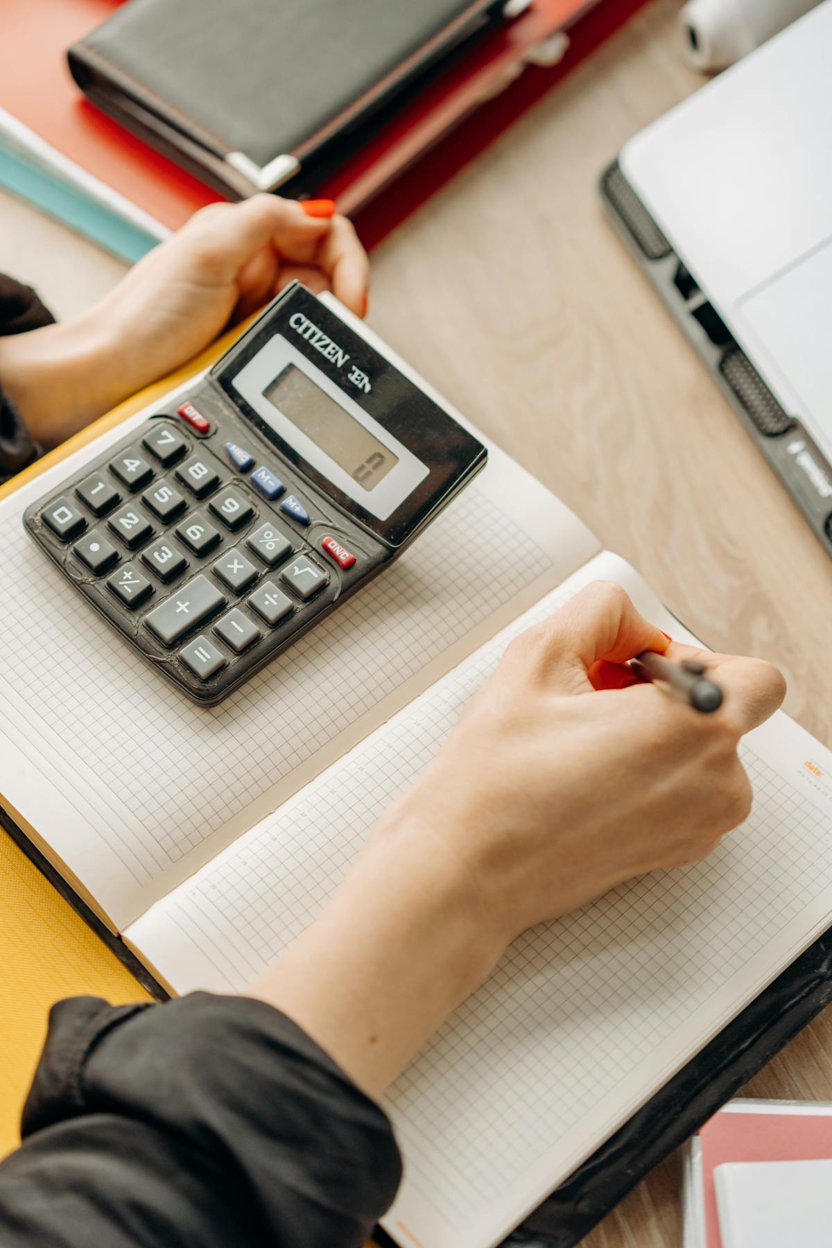 A hand writing in a notebook beside a calculator.