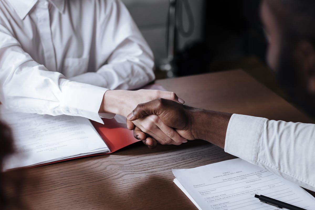 A handshake across documents on a desk.